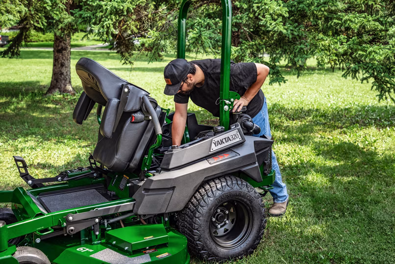 Man checking Yakta 320 zero-turn mower with reinforced steel deck and durable design